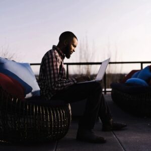 A man sitting on top of a chair using a laptop.