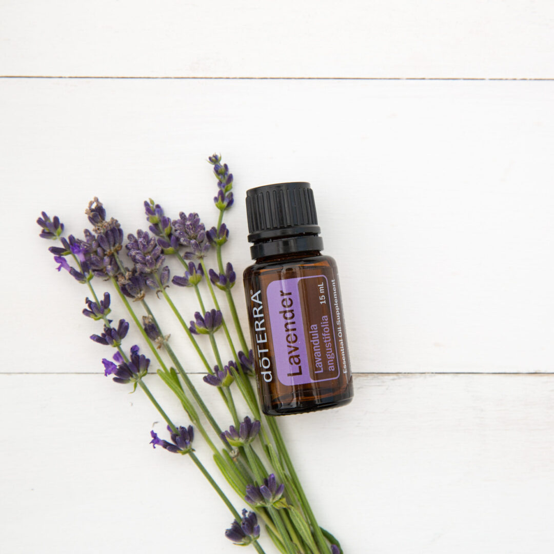 A bottle of lavender oil next to some purple flowers.